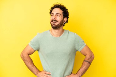 Genç sakallı adam mutlu, neşeli ve kendinden emin görünüyor. Gururla gülümsüyor ve iki elini de kalçasında istiyor.