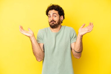 Genç sakallı adam şaşkın ve şaşkın hissediyor, şüpheci, farklı seçenekleri tartıyor veya komik bir ifadeyle seçiyor.