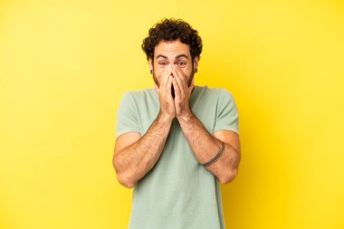 Genç sakallı adam mutlu, neşeli, şanslı ve şaşkın görünüyor. İki eliyle ağzını kapatıyor.