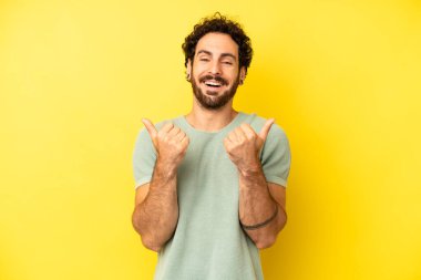 Genç sakallı adam neşeyle gülümsüyor ve mutlu görünüyor, kaygısız ve pozitif hissediyor.