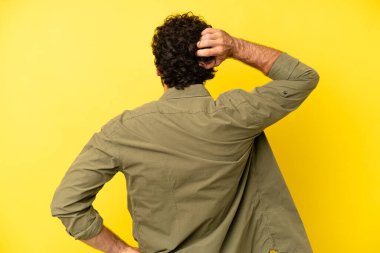 Genç sakallı adam düşünüyor ya da şüphe ediyor, kafasını kaşıyor, kafası karışık ve kafası karışık hissediyor, arkaya ya da arkaya bakıyor.