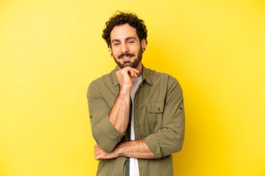 Genç sakallı adam gülümsüyor, hayattan zevk alıyor, mutlu, arkadaş canlısı, tatmin olmuş ve tasasız.