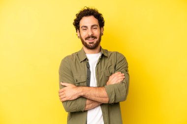 Genç sakallı adam mutlu, gururlu ve tatmin olmuş görünüyor. Kollarını kavuşturup gülümsüyor.