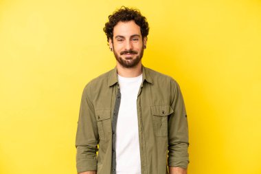 Genç sakallı adam, olumlu ve kendinden emin gülümsüyor. Tatmin olmuş, arkadaş canlısı ve mutlu görünüyor.