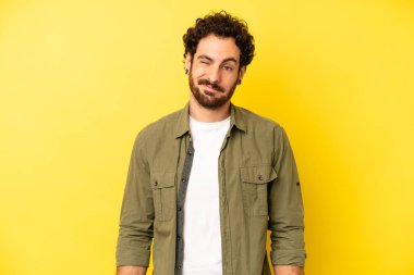 Genç sakallı adam mutlu ve arkadaş canlısı görünüyor, gülümsüyor ve sana olumlu bir tavırla göz kırpıyor.