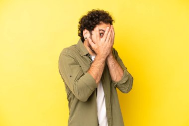 Genç sakallı adam korkmuş ya da utanmış hissediyor, gözleri yarı kapalı ya da elleri kapalı gözetliyor.