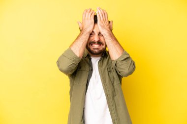 Genç sakallı adam stresli ve endişeli, depresif ve hayal kırıklığına uğramış hissediyor, iki elini de başa kaldırıyor.