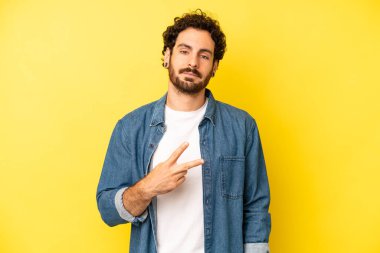 Genç sakallı adam mutlu, pozitif ve başarılı hissediyor, göğsünde el yapımı V ile, zafer ya da barış gösteriyor.