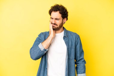 Genç sakallı adam yanağını tutuyor ve acı veren diş ağrısı çekiyor, hasta, sefil ve mutsuz hissediyor, dişçi arıyor