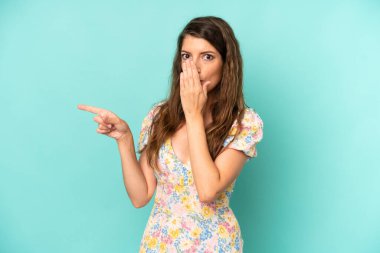 Genç, güzel bir kadın kendini mutlu, şaşkın ve şaşırmış hissediyor. Ağzını eliyle kapatıyor ve yanal fotokopi alanını işaret ediyor.