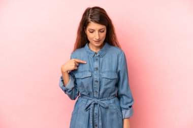 Genç ve güzel bir kadın neşeyle gülümsüyor, yere bakıyor ve göğsüne işaret ediyor.