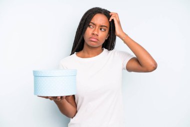 Kafası karışmış, kafası karışmış, kaşınan güzel siyah bir kadın. hediye kutusu konsepti