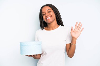 Siyah, güzel bir kadın mutlu bir şekilde gülümsüyor, el sallıyor, sizi selamlıyor ve selamlıyor. hediye kutusu konsepti