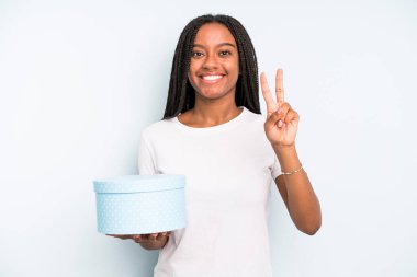 Siyah, güzel bir kadın gülümsüyor ve arkadaş canlısı görünüyor. İki numarayı gösteriyor. hediye kutusu konsepti