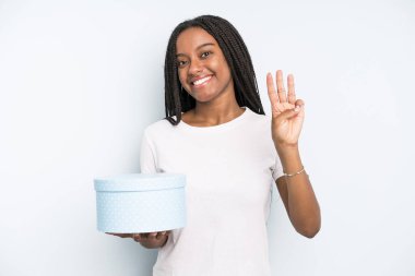 Siyah, güzel bir kadın gülümsüyor ve arkadaş canlısı görünüyor, üç numarayı gösteriyor. hediye kutusu konsepti