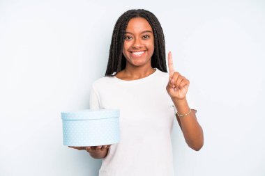 Siyah, güzel bir kadın gülümsüyor ve arkadaş canlısı görünüyor. Bir numarayı gösteriyor. hediye kutusu konsepti