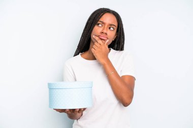 Siyahi güzel kadın düşünüyor, kuşkulu ve şaşkın hissediyor. hediye kutusu konsepti