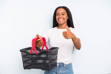 black pretty woman feeling proud,smiling positively with thumbs up. empty shopping basket