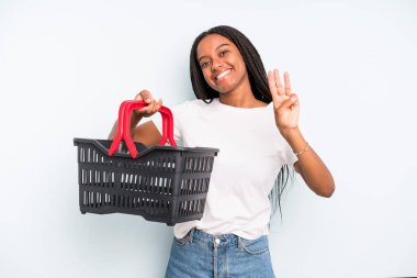 black pretty woman smiling and looking friendly, showing number three. empty shopping basket