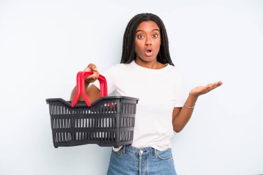 black pretty woman looking surprised and shocked, with jaw dropped holding an object. empty shopping basket