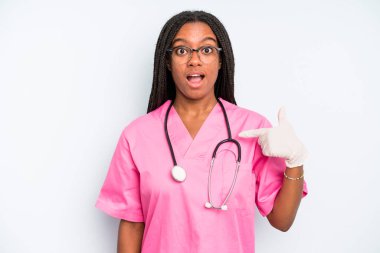black pretty woman looking shocked and surprised with mouth wide open, pointing to self. nurse concept