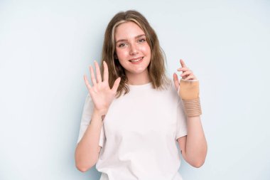 caucasian pretty woman smiling and looking friendly, showing number five. broken hand concept