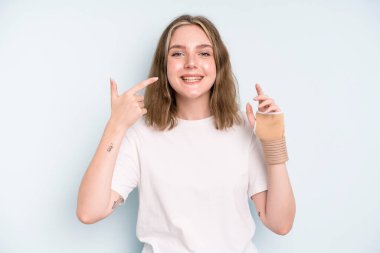 caucasian pretty woman smiling confidently pointing to own broad smile. broken hand concept