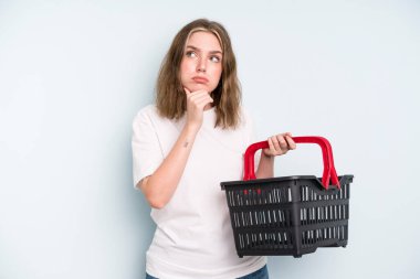caucasian pretty woman thinking, feeling doubtful and confused. empty shopping basket concept