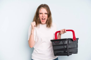 caucasian pretty woman shouting aggressively with an angry expression. empty shopping basket concept