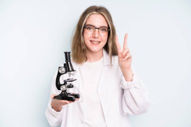caucasian pretty woman feeling happy, showing approval with okay gesture. science student with a microscope