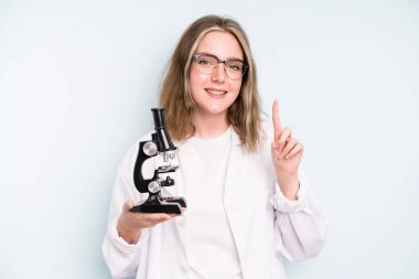 caucasian pretty woman smiling happily, waving hand, welcoming and greeting you. science student with a microscope