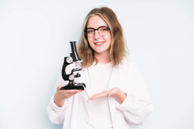 caucasian pretty woman smiling cheerfully, feeling happy and pointing to the side. science student with a microscope