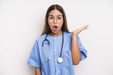 hispanic pretty woman looking surprised and shocked, with jaw dropped holding an object. medicine student concept