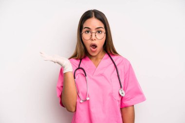 hispanic pretty woman looking surprised and shocked, with jaw dropped holding an object. medicine student concept