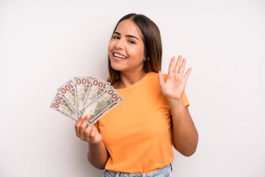 hispanic pretty woman smiling happily, waving hand, welcoming and greeting you. dollar banknotes savings concept