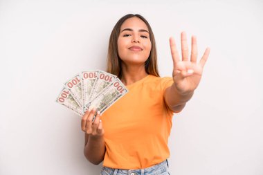 hispanic pretty woman smiling and looking friendly, showing number four. dollar banknotes savings concept