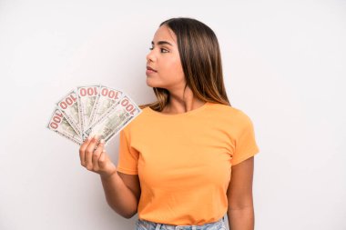 hispanic pretty woman on profile view thinking, imagining or daydreaming. dollar banknotes savings concept