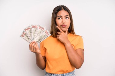 hispanic pretty woman thinking, feeling doubtful and confused. dollar banknotes savings concept