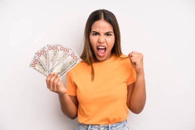 hispanic pretty woman shouting aggressively with an angry expression. dollar banknotes savings concept
