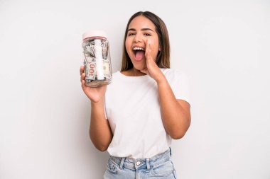 hispanic pretty woman feeling happy,giving a big shout out with hands next to mouth. dollar banknotes savings concept