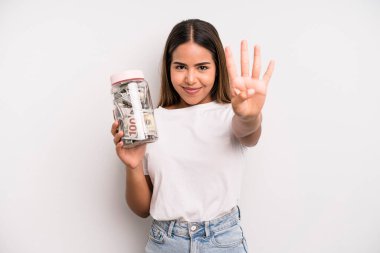 hispanic pretty woman smiling and looking friendly, showing number four. dollar banknotes savings concept