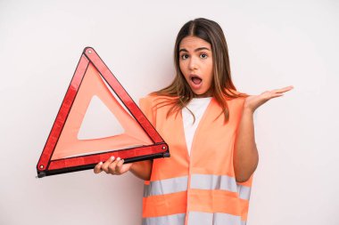 hispanic pretty woman looking surprised and shocked, with jaw dropped holding an object. car accident emergency concept