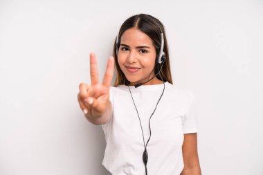 hispanic pretty woman smiling and looking happy, gesturing victory or peace. telemarketer concept