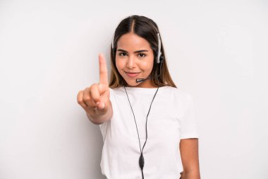 hispanic pretty woman smiling and looking friendly, showing number one. telemarketer concept