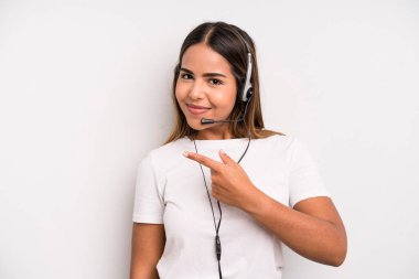 hispanic pretty woman smiling cheerfully, feeling happy and pointing to the side. telemarketer concept
