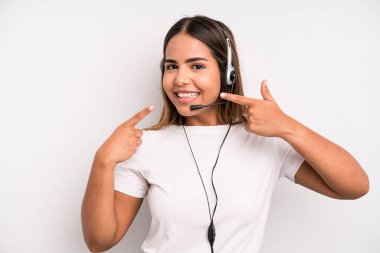 hispanic pretty woman smiling confidently pointing to own broad smile. telemarketer concept
