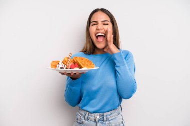 hispanic pretty woman feeling happy,giving a big shout out with hands next to mouth. waffles and breakfast concept