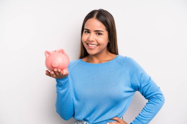 İspanyol güzel kadın mutlu bir şekilde gülümsüyor, eli kalçasında ve kendinden emin. Domuz kumbarası konsepti