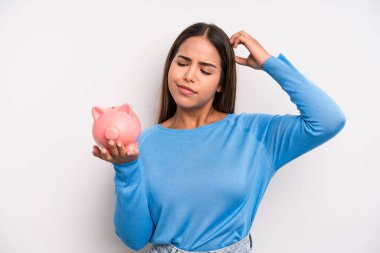 İspanyol güzel kadın şaşkın ve kafası karışık, kaşınan bir kafa hissediyor. Domuz kumbarası konsepti