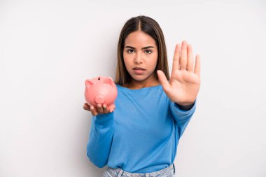 İspanyol güzel kadın ciddi görünüyor. Avuç içini gösteriyor. Durdurma hareketi yapıyor. Domuz kumbarası konsepti